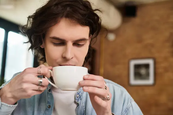 Young man savors his coffee in a relaxed atmosphere at his favorite cafe, enjoying the moment. — Stock Photo