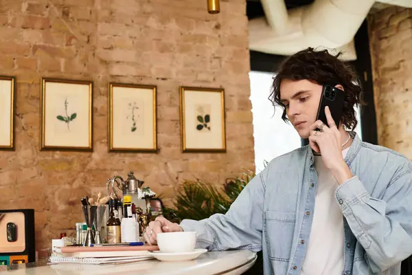 In a quaint cafe, a young and handsome man engages in a phone conversation while savoring a cup. — Stock Photo
