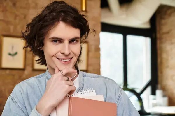 In a cozy cafe, a young handsome man holds his notebooks, smiling as he enjoys his leisure time. — Stock Photo