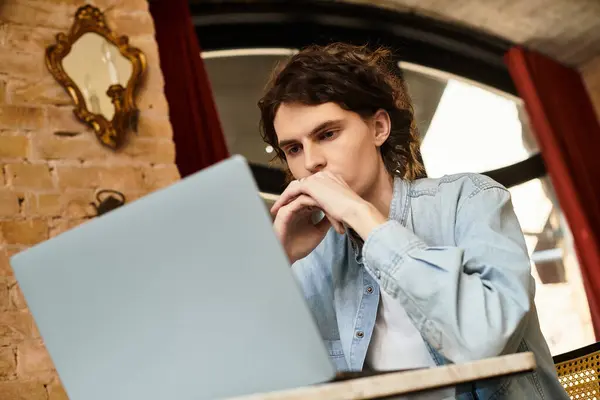 Handsome young man sits at a cafe table, deeply engaged with his laptop and surroundings. — Stock Photo