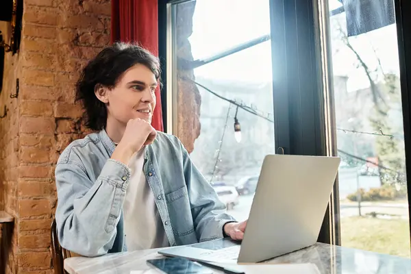 A young man sits at a cafe, smiling and focused on his laptop as he enjoys his free time. — Stock Photo