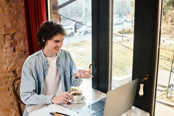 A young, handsome guy at a cafe smiles while sipping coffee and using his laptop. — Stock Photo