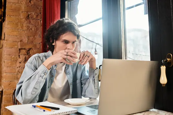 Handsome young man sips coffee at a cafe, focused on his laptop in a relaxed atmosphere. — Stock Photo