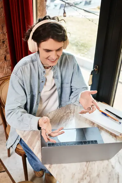 Young handsome guy interacts animatedly with friends online while seated comfortably at a cafe. — Stock Photo