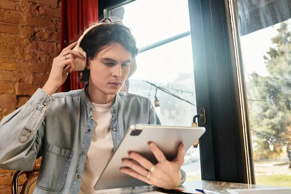 Handsome young guy sits at a cafe table, focused on his tablet as he relaxes with music. — Stock Photo