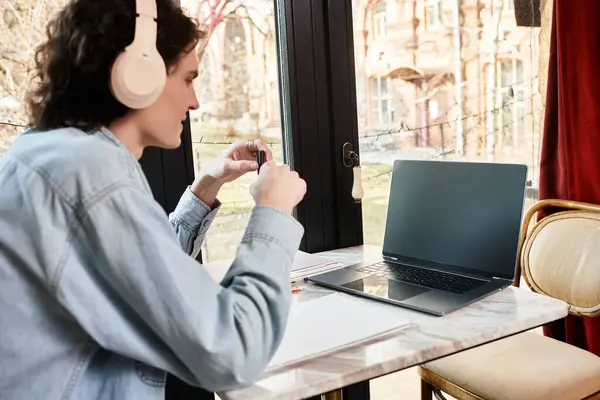 Handsome young guy relaxes at a cafe, focused on his tasks with headphones on, surrounded by charm. — Stock Photo