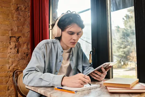 In a cozy cafe, a young handsome guy focuses on writing while listening to music on his headphones. — Stock Photo