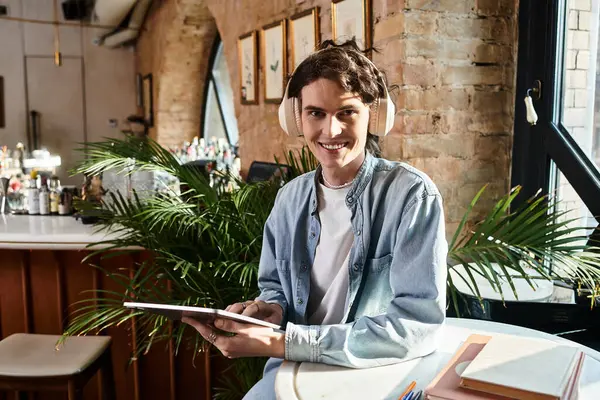 Handsome young guy relaxes at a cafe, wearing headphones and engaging with a tablet device. — Stock Photo