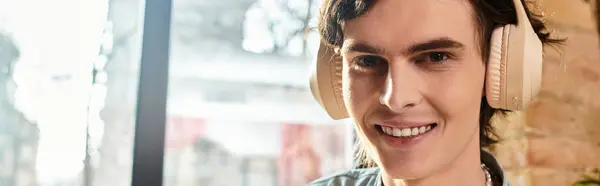 A young, attractive man sits at a cafe, smiling and enjoying leisure time with headphones on. — Stock Photo