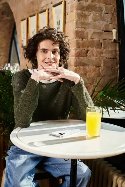 A handsome young man relaxes at a cafe table, enjoying a cool drink. — Stock Photo