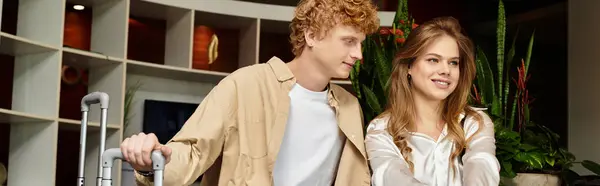 Una joven pareja sonríe y se abraza mientras se registra en un hotel moderno, mostrando su amor. - foto de stock