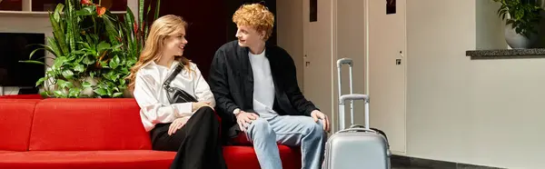 A lovely young couple relaxes on a vibrant red couch, sharing smiles and laughter in a hotel lobby. — Stock Photo