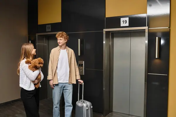A happy couple by the hotel elevators embraces their cute dog, enjoying their time together. — Stock Photo