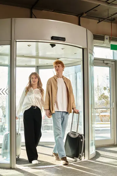 A young couple smiles as they carry luggage through a hotels revolving door — Stock Photo