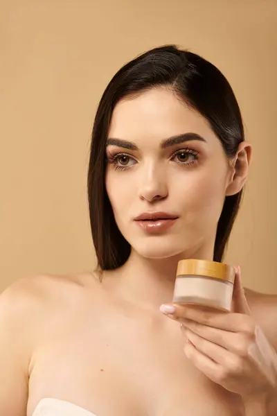 Mujer joven con la piel brillante sostiene un producto para el cuidado de la piel, exudando confianza y belleza. - foto de stock