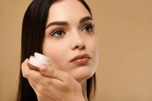 In a studio setting, a young woman highlights her healthy, glowing skin while applying skin care. — Stock Photo