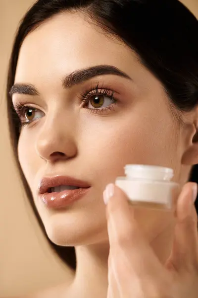 Young woman applies skincare, highlighting her radiant, healthy complexion in a bright studio. — Stock Photo