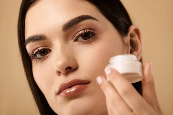 A young woman gently applies skincare cream, highlighting her radiant and healthy look. — Stock Photo