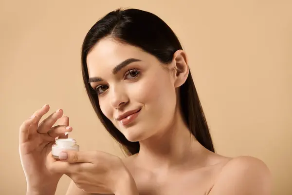A young woman showcases her exquisite skin while applying skincare in a bright studio. — Stock Photo
