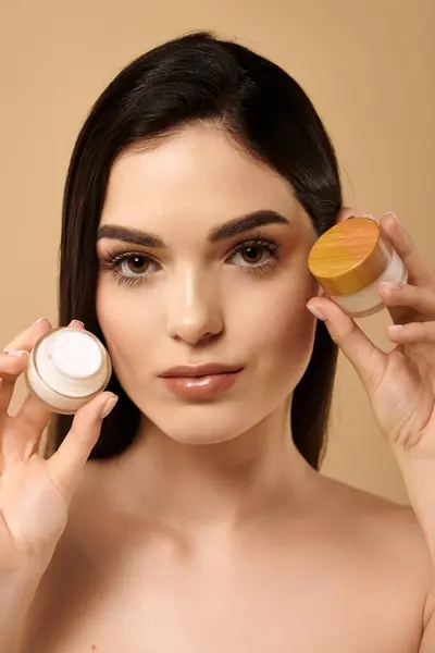 A young woman displays her glowing skin while holding skincare products in a studio setting. — Stock Photo