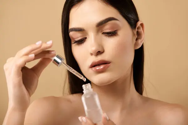 A young woman applies a serum with focus on her radiant skin, showcasing beauty techniques. — Stock Photo