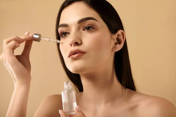 Young woman applies a serum to enhance her radiant, healthy complexion in a studio setting. — Stock Photo