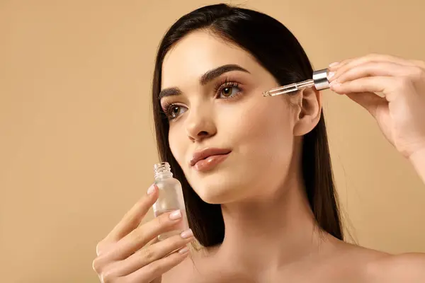 A young woman showcases her radiant skin while applying skincare serum, highlighting beauty. — Stock Photo