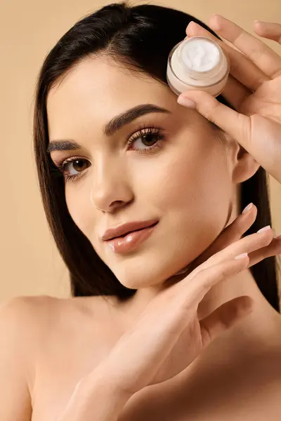 A young woman with stunning skin demonstrates her beauty regimen in a well-lit studio. — Stock Photo