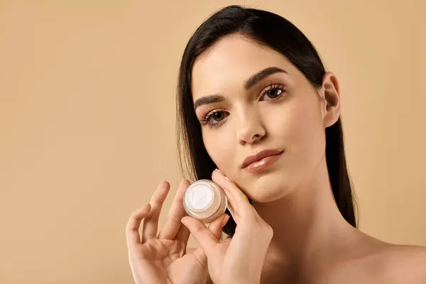 Jeune femme séduisante démontre une peau brillante parfaite tout en tenant la crème de soin en studio. — Photo de stock