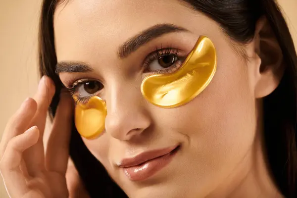 A young woman showcases her radiant skin while applying skincare products in a calm studio. — Stock Photo