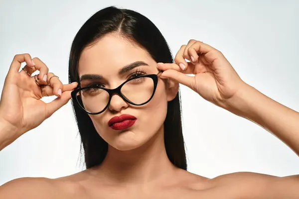 A confident young woman poses with glasses, showcasing her bold red lips and brown hair. — Stock Photo