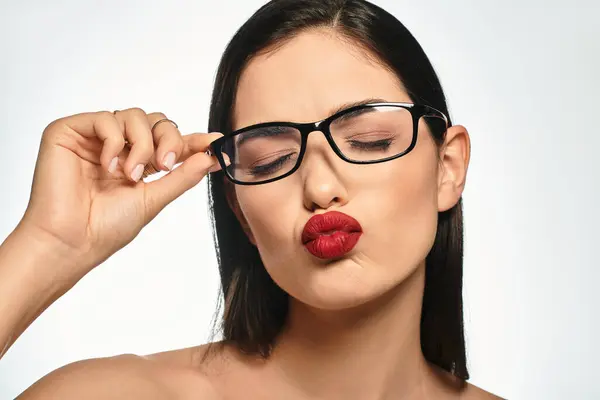 A beautiful young woman playfully poses with glasses, showcasing her stunning makeup and red lips. — Stock Photo