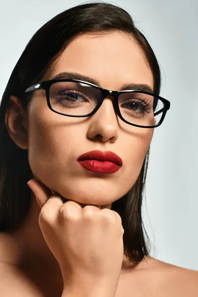 A young woman with brown hair poses confidently against a grey backdrop, showcasing her red lips. — Stock Photo