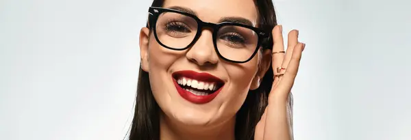 Brown-haired woman smiles, showing red lips and stylish glasses in a simple setting, banner — Stock Photo