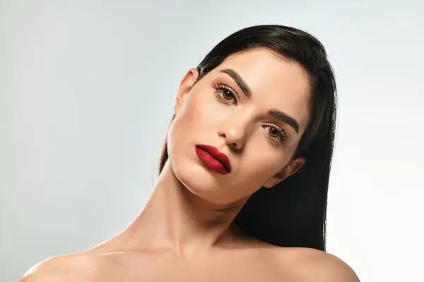 A stunning young woman with brown hair and striking red lips gazes confidently at the camera. — Stock Photo