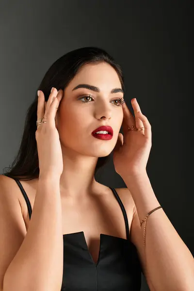 Uma jovem mulher com cabelo castanho bonito toca suavemente o rosto enquanto mostra lábios vermelhos vibrantes. — Fotografia de Stock