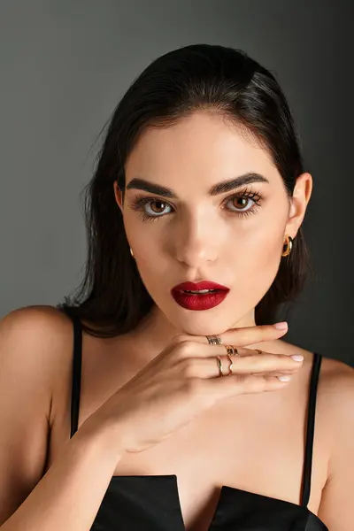 A stunning young woman with brown hair and vibrant red lips poses elegantly against a grey backdrop. — Stock Photo