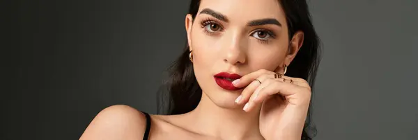 A young woman with brown hair and red lips poses beautifully against a grey background, banner — Stock Photo