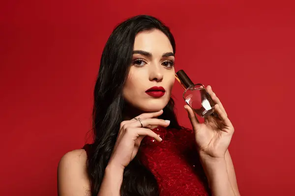 A young woman holds a perfume bottle elegantly in a colorful studio. — Stock Photo