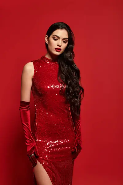 Una hermosa joven posa graciosamente en un estudio con un vestido rojo brillante y guantes. - foto de stock