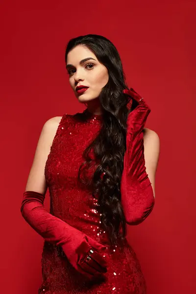 A beautiful woman with long brown hair poses gracefully, wearing red lipstick and a sparkling dress. — Stock Photo