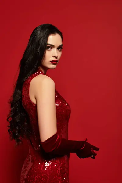 A captivating young woman with brown hair and red lips poses gracefully in a striking red outfit. — Stock Photo
