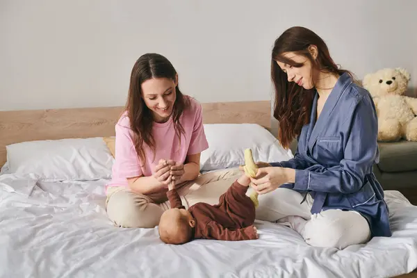 Two loving mothers enjoy time with their baby in a cozy bedroom on Mothers Day. — Stock Photo