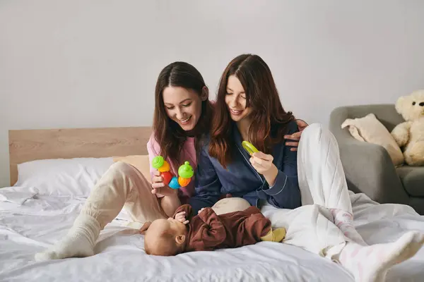 Two smiling mothers share a tender moment with their baby, surrounded by warmth and love at home. — Stock Photo