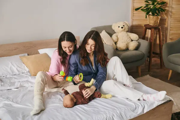 Two mothers joyfully play with their baby at home on Mothers Day. — Stock Photo