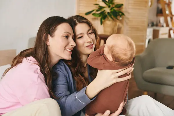 Two loving mothers share a joyful moment with their child in a cozy home on Mothers Day. — Stock Photo