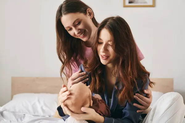 Two moms joyfully embrace their child in a cozy home, celebrating Mothers Day together. — Stock Photo