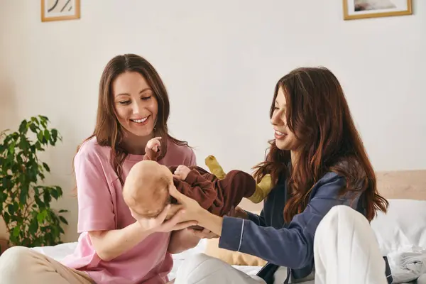 Deux mères aimantes chérissent des moments avec leur enfant, créant une atmosphère familiale chaleureuse à la maison. — Photo de stock
