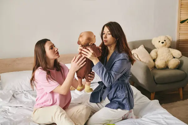 Two loving mothers share a tender moment with their child in a cozy bedroom on Mothers Day. — Stock Photo