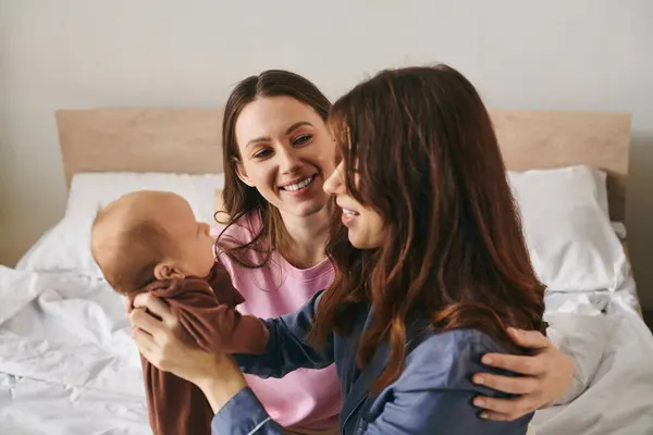 Two loving mothers share a heartwarming moment with their baby in a cozy bedroom setting — Stock Photo